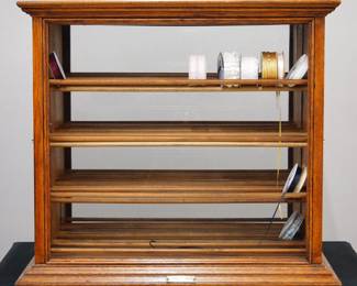 A turn of the century A.N. Russell & Sons Ribbon Cabinet. Oak construction with glass front and back that features four vertical pull out racks, each with four shelves. Brass plaque at the base that reads "Manuf'd by A.N. Russell & Sons Ilion., N.Y. U.S.A.". Older refinish with some wear, front glass appears to be replacement, back is original (wavy). 29 x 23 1/2 x 25 1/2" high overall. ESTIMATE $400-600