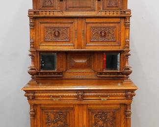 A late 19th century Victorian sideboard. Oak construction with hand carved panels and spindle work galleries features a hooded upper section with a molded cornice over an open shelf and two paneled doors over an open serving area with central panel and beveled side mirrors and turned columns, molded base over two dovetailed drawer flanked by carved masks over two paneled doors flanked by turned fluted columns and lower molded base. Older finish with some wear, lacks several small parts including the upper gallery spindles, some finials and small moldings. 51 x 23 x 86 1/2" high overall. ESTIMATE $800-1,200