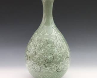 A Korean Goryeo-style Celadon porcelain vase. Bottle form with a flared rim, decorated with cranes, clouds, and medallions below a lotus leaf band in a crackle glaze. Marked at the underside. Repair at the rim, approximately 1 x 1/2", light wear overall. ESTIMATE $600-800