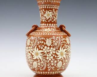 A turn of the century Thun Art Pottery vase. Amphora form with two ring handles and applied White floral design on an Orange ground. Applied "Thun" lozenge mark and paper "Made in Switzerland" label. Minor wear, a few small flakes to decoration and foot. 9 3/4" high. ESTIMATE $100-150
