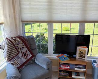 Phillips flatscreen TV on TV stand, recliner, chair, nice throw and books.