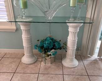 Elegant glass console featuring a thick beveled glass top supported by two classical column pedestals. A beautiful statement piece for an entryway, foyer, dining room, or coastal-inspired home. Quality décor and coordinating accessories throughout the home will also be available.