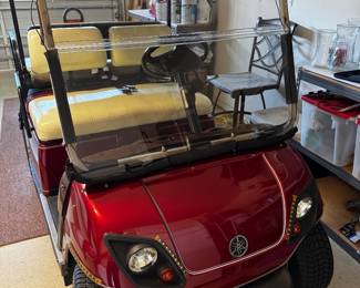 Yamaha Gas Golf Cart finished in a rich metallic burgundy with cream upholstery. This well-maintained cart features comfortable 4-passenger seating, a fold-down rear seat with cargo deck, custom alloy wheels, full windshield, sun top, woodgrain-style dashboard with multiple cup holders, seat belts, and headlights. A dependable gas-powered cart that’s perfect for cruising The Villages or around the neighborhood.