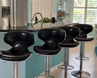Set of four contemporary black adjustable swivel bar stools featuring chrome pedestal bases, footrests, and cushioned seats with backrests. Perfect for a kitchen island, breakfast bar, game room, or entertaining space.