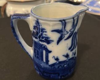 Doulton England Blue Willow Creamer — This charming Doulton England creamer features the classic Blue Willow pattern, known for its intricate blue and white oriental design. Made of fine porcelain, this piece measures approximately 3.5 inches tall and 4 inches in length including the spout. The creamer is in good condition with some minimal signs of use but no visible chips or cracks. Its delicate craftsmanship and timeless pattern make it a lovely addition to any Blue Willow or vintage dish collection. Marked on the bottom with the Doulton maker's mark, it carries authentic English heritage.