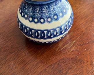 Blue and White Small Ceramic Vase — This charming small ceramic vase features a classic blue and white looped pattern around its rounded body. Crafted from glazed ceramic, the piece is ideal for decorative display or holding small floral arrangements. Measuring approximately 3 inches in height and 3.5 inches in diameter, this vase fits easily on small tables or shelves. It is in good condition with a visible fine hairline crack on one side, adding character without compromising its overall appeal. Perfect for collectors of handmade or vintage-style pottery.