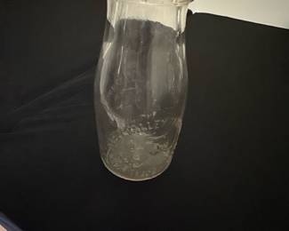 Happy valley Dairy Clear Glass Milk Bot — This vintage Crowley Farm Dairy milk bottle features clear glass embossed with a farm scene including a cow and lettering. The bottle has a narrow neck with a rounded lip and stands as a collectible piece of dairy history. It measures approximately 8.25 inches tall and 3.25 inches wide, making it a classic size for milk bottles from the mid-20th century. The item is in good condition with some wear consistent with age, including minor cloudiness and light surface marks but no chips or cracks. This piece represents a charming relic of traditional dairy farming, perfect for collectors or rustic decor enthusiasts.