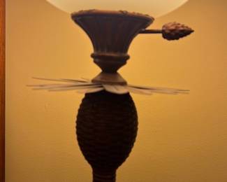 Brown Pineapple Torchiere Floor Lamp — This distinctive pineapple-themed torchiere floor lamp features a textured brown base and post, topped with a wide opaque glass shade that diffuses light warmly. The lamp's height and slim design make it suitable as an accent piece in a dining room or living space. Measuring approximately 65 inches tall and 15 inches wide at the shade, it offers ambient lighting with a classic decorative appeal. It is in good condition with minor surface wear consistent with regular use but no visible damage. Its traditional style and unique pineapple motif make it a charming addition to home decor collections.