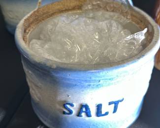 Blue Ceramic Salt Crock — This charming blue ceramic salt crock is a classic addition to any kitchen collection. It features a glazed finish with the word 'SALT' embossed on the front, and a practical hanging tab for easy placement. The crock measures approximately 4 inches tall by 4.5 inches wide and 3.5 inches deep, making it a convenient size for countertop or wall use. It is in good condition with no visible chips or cracks. Ideal for storing salt in a functional and decorative way.