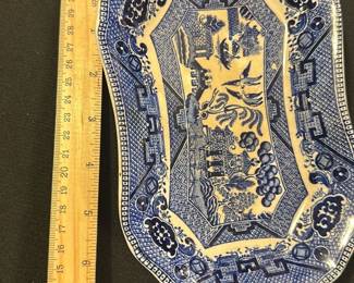 Semi-Vitreous Blue Willow Dish — This charming semi-vitreous dish features the iconic Blue Willow pattern in classic blue and white. Crafted from ceramic with a semi-vitreous finish, it displays traditional Chinese-inspired motifs including pagodas, bridges, and willow trees framed by a decorative patterned border. Measuring approximately 11.5 inches in length and 7.5 inches in width, it is a versatile serving or decorative piece. The dish is in good condition with minor surface wear and some glaze imperfections typical of vintage ceramics. The maker's mark on the bottom confirms its semi-vitreous composition and adds to its collectible appeal.