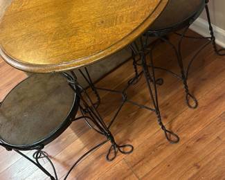 Heartback Metal Bistro Set — This charming bistro set features a metal frame with intricately twisted wirework forming heart-shaped backs on the chairs. The round wooden tabletop displays a warm natural finish, paired with cushioned seats covered in dark fabric. Measuring approximately 28 inches in height and 24 inches in table diameter, this set is perfect for small spaces or cozy corners. The sturdy iron construction and classic design remain in good condition with minor wear consistent with light use. Ideal for basement or patio use, it combines vintage romantic style with functional seating and dining space.