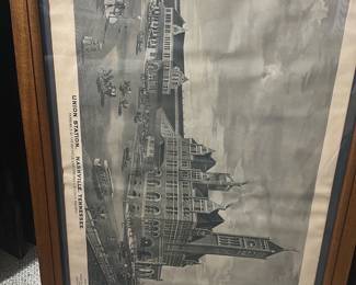 Union Station Nashville Print — Framed lithographic print depicting Union Station, Nashville, Tennessee (terminals of the Nashville, Chattanooga & St. Louis Railway). The piece is matted and set in a simple oak-tone wooden frame with glass, showing architectural detail of the historic station in grayscale. Overall size is moderate and suitable for wall display in a bonus room or office; frame shows light surface wear and the paper has mild age-toning and a small crease near the top edge. Good estate-sale condition for display with no major tears to the image; glass and frame are intact though the frame has minor scuffs consistent with normal use.