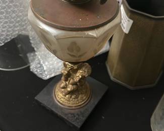 Vintage Cherub Glass Oil Lamp — This vintage oil lamp features a charming cherub base in a gold-tone finish, adding a whimsical touch to any room. The lamp has a frosted glass font with floral etching and an original glass chimney. Standing approximately 15 inches tall, it combines decorative elegance with functional design. The base exhibits some wear consistent with age, and the glass chimney shows minor dirt but no cracks. Ideal for collectors or those seeking a unique vintage decorative piece.
