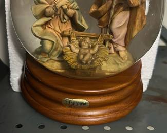 Fontanini Nativity Musical Globe — This Fontanini musical nativity globe features a detailed resin holy family scene inside a clear globe mounted on a turned wood-tone base. The piece is marked "Fontanini" on a metal label on the base and appears to be the boxed musical decoration often sold for holiday display. Measures approximately 9 inches tall with a 6.5 inch globe diameter and sits on a 6.5 inch round base. Overall good condition with light surface wear to base and no visible cracks in the globe; original box pictured but may show storage wear.