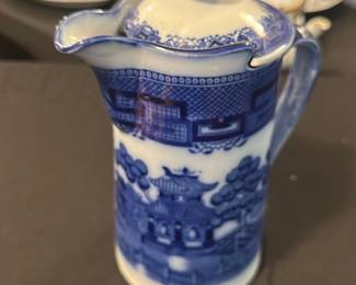 Burslem England Blue Willow Pitcher — This charming Burslem England pitcher features the classic Blue Willow pattern, renowned for its intricate blue and white design. Crafted from fine porcelain, it includes a fitted lid and a gracefully curved spout and handle, perfect for serving beverages. The pitcher measures approximately 6 inches tall and 4 inches wide, making it a compact and elegant addition to any collection or table setting. It is in good condition with minor signs of use consistent with age and no visible chips or cracks. Marked with the Burslem England hallmark and the Blue Willow stamp, this piece reflects traditional English ceramic craftsmanship.