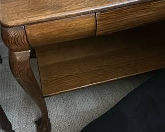 Oak Wood Queen Anne Style Table — This elegant oak wood table features Queen Anne style cabriole legs with claw feet, offering a classic and refined look. The rich wood grain is visible throughout, complemented by a smooth rectangular top and a functional lower shelf for additional storage or display. The piece includes a small drawer with dovetail joints, enhancing both utility and craftsmanship. It measures approximately 24 inches high, 26 inches wide, and 18 inches deep, making it suitable for bedroom or living room use. The table is in good condition with typical light surface wear and minor scratches consistent with age and use.