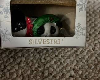 Silvestri Panda Christmas Ornament — Silvestri panda Christmas ornament in original display box, featuring a hand-painted panda wearing a green wreath and red bow. The resin/ceramic ornament is shown in its white box with snowflake motif and viewing window, making it ready for gifting or display. Small tabletop ornament approximately the size of a typical holiday tree decoration and lightweight for easy hanging or shelf display. Box shows light shelf wear and creasing but ornament appears intact with no visible chips or paint loss.