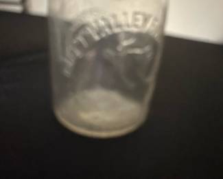 Happy valley Dairy Clear Glass Milk Bot — This vintage Crowley Farm Dairy milk bottle features clear glass embossed with a farm scene including a cow and lettering. The bottle has a narrow neck with a rounded lip and stands as a collectible piece of dairy history. It measures approximately 8.25 inches tall and 3.25 inches wide, making it a classic size for milk bottles from the mid-20th century. The item is in good condition with some wear consistent with age, including minor cloudiness and light surface marks but no chips or cracks. This piece represents a charming relic of traditional dairy farming, perfect for collectors or rustic decor enthusiasts.