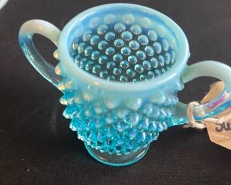 Blue Hobnail Glass Sugar Bowl — This charming blue hobnail glass sugar bowl features a distinctive textured pattern with raised knobs and a delicate opalescent gradient from light to deeper blue. The bowl includes two elegant handles and sits on a small round base, perfect for vintage or antique glassware collectors. Measuring approximately 3.5 inches in height and 4.5 inches in width, it fits nicely on a tea or coffee table. It is in excellent condition with no visible chips, cracks, or damage. This piece adds a touch of classic elegance to any master bedroom or dining set.