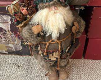 Brown Fabric Santa Figurine — Rustic brown fabric Santa figurine dressed in felt and faux-fur with a wreath-trimmed hat and a bundle of pinecone/berry decorations. Detailed with a curly white beard, mittened hands, rope belt, and stitched boots for a handcrafted cottage look. Stands approximately 18 inches tall (estimated) and is suited for tabletop or floor holiday display in the Office Up Room. Good condition with light shelf wear and intact trim; some natural-looking distressing consistent with its rustic style.
