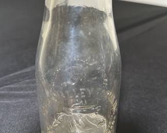 Happy valley Dairy Clear Glass Milk Bot — This vintage Crowley Farm Dairy milk bottle features clear glass embossed with a farm scene including a cow and lettering. The bottle has a narrow neck with a rounded lip and stands as a collectible piece of dairy history. It measures approximately 8.25 inches tall and 3.25 inches wide, making it a classic size for milk bottles from the mid-20th century. The item is in good condition with some wear consistent with age, including minor cloudiness and light surface marks but no chips or cracks. This piece represents a charming relic of traditional dairy farming, perfect for collectors or rustic decor enthusiasts.