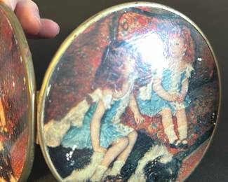 Vintage Double-Sided Round Compact Mirro — This vintage double-sided round compact mirror features a charming printed image of two girls in blue dresses with a dog, capturing a nostalgic scene on the exterior. The compact is crafted from metal with a brass tone finish, offering two functional mirrors within its hinged design. Measuring approximately 3.5 inches in diameter, it is a delicate and portable accessory suitable for personal use or display. The item shows signs of wear on the printed image but remains structurally intact and fully functional. Ideal as a collectible or a vintage beauty accessory.
