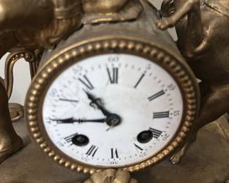 Antique Gilt Mantel Clock Figurine — This antique gilt mantel clock features an elaborate figurine of a seated hunter with dogs and a bird, showcasing intricate craftsmanship and artistic detail. The clock has a white enamel dial with Roman numerals and is set within an ornately decorated gilt metal case accented with black panels and floral motifs. Measuring approximately 16 inches in height, 14 inches in width, and 6 inches in depth, this clock is a striking decorative timepiece suitable for a traditional bedroom or living room. The clock shows some wear on the dial consistent with age, and the gilt finish has minor patina that adds character. A distinctive collectible piece typical of 19th-century French-style mantel clocks.
