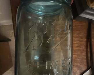 Ball Perfect Mason Blue Canning Jar — This vintage Ball Perfect Mason jar in blue glass is a classic collectible for canning and storage. Featuring the iconic Ball logo embossed on the front, the jar includes an original metal screw lid with a red rubber sealing ring for airtight closure. The jar measures approximately 7 inches in height and 4 inches in diameter, making it ideal for a variety of kitchen or decorative uses. It is in good condition with minor wear on the lid consistent with age but no cracks or chips in the glass. A prized item for vintage kitchenware collectors, it represents early 20th-century American glass craftsmanship.