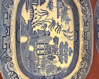 Blue Willow Platter — This vintage Buffalo Pottery blue willow platter dated 1909 features a classic semi-vitrous ceramic construction with intricate blue scenic patterns typical of the willow design. The platter measures approximately 12 inches wide and 15.5 inches long, making it a versatile serving dish or decorative piece. It displays a lovely crackle glaze consistent with its age but remains in good condition with no visible chips or cracks. The iconic buffalo logo and date stamp confirm its authenticity and add historical value to this collectible pottery piece.
