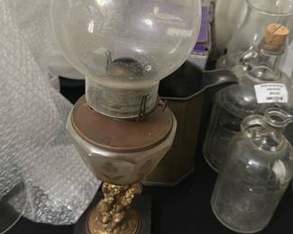 Vintage Cherub Glass Oil Lamp — This vintage oil lamp features a charming cherub base in a gold-tone finish, adding a whimsical touch to any room. The lamp has a frosted glass font with floral etching and an original glass chimney. Standing approximately 15 inches tall, it combines decorative elegance with functional design. The base exhibits some wear consistent with age, and the glass chimney shows minor dirt but no cracks. Ideal for collectors or those seeking a unique vintage decorative piece.