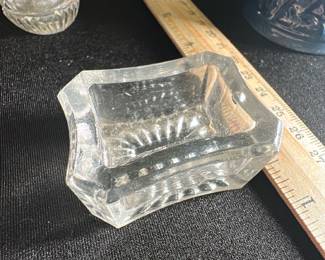 Clear Glass Salt Cellar Dish — This clear glass salt cellar dish features a classic rectangular shape with scalloped sides and a textured starburst pattern on the base. Crafted from thick clear glass, it provides an elegant and functional table accessory. Measuring approximately 2.5 inches wide, 1.5 inches high, and 2.5 inches deep, this small dish is ideal for holding salt or spices during meals. The item is in good vintage condition with minor surface wear typical for its age. A charming addition for collectors or those seeking vintage dining accessories.