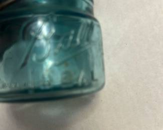 Ball Aqua Glass Jar with Wire Bale — This vintage Ball glass jar features a distinctive aqua blue color and a wire bale closure, typical of early 20th-century canning jars. Made from thick glass, it includes embossed Ball branding and a patent date indicating its collectible nature. Measuring approximately 4 inches in height and 3 inches in diameter, it is a sturdy piece suitable for display or storage. The jar is in good condition with signs of use and some minor wear to the wire bale closure. A great addition for collectors of vintage kitchenware or rustic home decor.