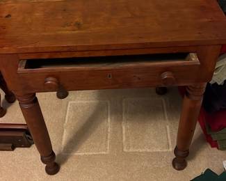 Antique Wood Side Table — This antique cherry wood side table features a sturdy rectangular top and a single drawer with wooden knobs and a keyhole. The piece stands on turned legs with bun feet, showcasing craftsmanship typical of the 19th century. Measuring approximately 30 inches in height, 28 inches in width, and 19 inches in depth, it offers practical use for bedroom or living areas. The table shows some wear consistent with age, including minor surface scratches and finish loss, but remains solid and stable. This charming piece brings classic vintage appeal and functional storage to any space.