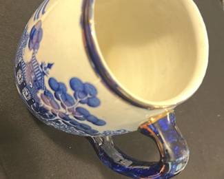 Buffalo Pottery Blue White Pitcher — This charming Buffalo Pottery pitcher features a classic blue and white design with a scenic pagoda and tree motif. Crafted from fine pottery and marked on the bottom with a Buffalo Pottery 1908 stamp, it measures approximately 7.5 inches tall. The pitcher is in good condition with light wear consistent with age and use. It is a timeless piece suited for collectors of vintage American pottery or those appreciating early 20th-century design.