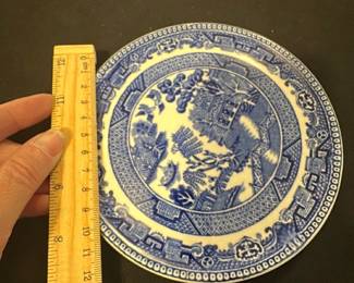 Wedgwood Blue & White — This classic Wedgwood blue and white plate features the traditional Willow pattern design, showcasing intricate scenes of pagodas, bridges, and foliage. Crafted from fine English porcelain, it displays the characteristic blue transfer print on a white background. Measuring approximately 7 inches in diameter, the plate is a lovely example of English decorative china. It shows some fine crazing but remains free from chips or cracks, preserving its vintage charm. Marked on the back with the Wedgwood & Co. England stamp, this plate embodies collectible English pottery craftsmanship.