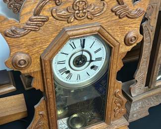 Antique Oak Mantel Clock — This antique oak mantel clock features intricate carved detailing on the case, highlighting craftsmanship typical of late 19th to early 20th century design. The clock face has Roman numerals behind a beveled glass door that reveals the pendulum inside. Measuring approximately 16 in height, 11 in width, and 5 in depth, this stately piece is a functional and decorative addition to any vintage or traditional home decor. The clock is in good working condition with minor wear consistent with age, preserving its authentic patina. Its detailed woodwork and classic design make it a collectible timepiece ideal for bedrooms or living rooms.