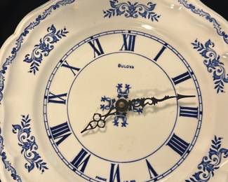 Bulova Blue White Wall Clock — This Bulova wall clock features a classic blue and white ceramic plate design with ornate Roman numerals and delicate floral motifs. Crafted in France, the clock combines vintage elegance with functional timekeeping, highlighted by intricately detailed black hands. Measuring approximately 11 inches in diameter, it is an ideal decorative and practical piece for any home. The clock is in good condition, showing minor signs of age-related wear consistent with vintage ceramics and working reliably. Its unique blend of decorative porcelain and precision clockwork makes it a charming collector's item.