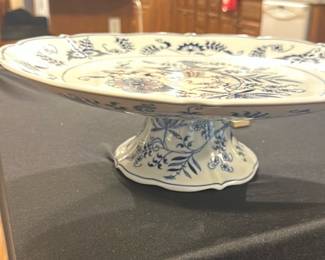 Blue Danube Pedestal Cake Plate — This elegant Blue Danube pedestal cake plate features a classic white base adorned with intricate blue floral patterns. Crafted in Japan, it showcases a delicate scalloped edge and sturdy footed base, perfect for serving cakes or desserts with style. Measuring approximately 10 inches in diameter and 4 inches tall, it adds a timeless touch to any dining setting. The plate is in excellent condition with no visible chips or cracks. A wonderful example of Blue Danube's charming design and quality craftsmanship.