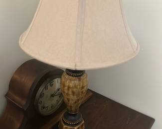 Table Lamp with Beige Shade — This rustic table lamp features a uniquely patterned wooden base with earthy brown tones and decorative accents. The lamp is topped with a beige fabric shade that softly diffuses light, making it ideal for a cozy bedroom setting. Measuring approximately 24 inches tall and 12 inches wide at the shade, it balances style and function perfectly. The lamp is in good condition with minor signs of use but fully functional. Its traditional design complements a variety of interior decor styles.