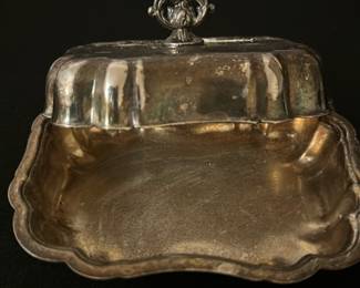 Vintage Silver plated Butter Dish — This vintage silver-plated butter dish features an elegant curved lid with a decorative finial handle. The tray has a scalloped edge and a polished interior, perfect for serving butter or small delicacies. Measuring approximately 3 inches high, 7 inches wide, and 5 inches deep, it is compact and functional for any table setting. The dish shows light tarnish and surface wear consistent with age but remains in good condition overall. A charming addition to vintage tableware collections or antique decor.