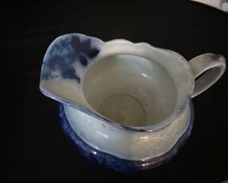 Waldorf Blue Creamer Pitcher — This Waldorf blue and white ceramic creamer pitcher is a charming addition to any vintage kitchen collection. Featuring a delicate, scalloped rim and a classic blue floral design on white glazed pottery, this piece is both decorative and functional. The pitcher stands approximately 3.5 inches tall with a width of 5 inches from spout to handle, and has a sturdy construction typical of historic English pottery. It is in good condition with some minor surface wear consistent with its age. Marked on the bottom with 'Waldorf England Ware'.