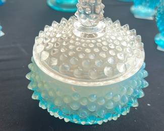 Fenton Blue Opalescent Hobnail  Dish — This stunning Fenton Blue Opalescent Hobnail Candy Dish features a beautiful textured hobnail pattern in a classic blue opalescent glass. The dish includes a matching lid with a pointed finial, showcasing the intricate hobnail design characteristic of Fenton glassware. Measuring approximately 4 inches in height and 5 inches in diameter, it is perfect for decorative or functional use. The piece is in excellent condition with no visible chips or cracks, preserving its vintage charm. A delightful collectible for lovers of antique and collectible glassware.