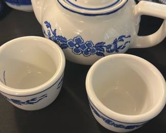 Jackson China Blue Floral Teapot Set — This charming Jackson China teapot set from Falls Creek, PA, features classic blue floral designs on white ceramic. The set includes a compact teapot with lid and two matching cups, all decorated with delicate blue floral motifs. The teapot measures approximately 4.5 inches in height and 8 inches in length including the handle and spout, with cups around 2.5 inches tall and 3 inches wide. The set is in good condition, showing minor usage wear with no chips or cracks visible. This vintage ceramic set is perfect for collectors or for adding a quaint touch to any kitchen or dining room.