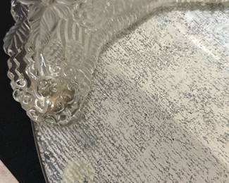 Vintage Glass Vanity Tray — This vintage glass vanity tray features intricately molded floral designs on both ends, highlighting a delicate and elegant style. The tray is constructed from thick glass with beveled edges and a distressed mirror finish that adds character. Measuring approximately 15 inches long, 7 inches wide, and 0.75 inches high, it is ideal for tabletop or dresser use. The tray shows expected wear with some minor spotting on the mirror surface consistent with age, but remains structurally sound. A charming addition to any vanity or decorative collection, it exudes classic vintage appeal.