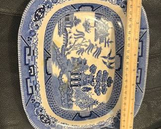 Blue Willow Semi-Vitreous Platter — This semi-vitreous blue willow platter features the classic blue and white transferware pattern with pagodas, trees, and birds. The platter measures approximately 12.5 inches in width and 10 inches in height, making it a versatile serving piece or decorative item. It shows signs of crazing consistent with age but remains structurally sound without visible chips or cracks. Ideal for collectors of vintage blue and white china, this platter adds a timeless touch to any table setting or display.