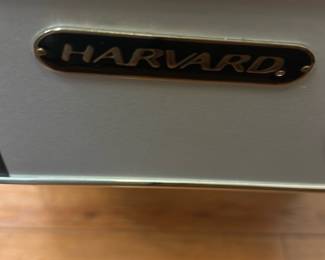 Harvard Air Hockey Table — This Harvard air hockey table combines classic arcade fun with durable construction and a sleek design. It features a white play surface with red and black markings, including the Harvard logo and name prominently displayed on both ends and center ice. The table measures approximately 84 inches in length, 42 inches in width, and 30 inches in height, making it suitable for home game rooms or recreational spaces. In good condition, it shows minor signs of use with clean playing surface and intact legs providing sturdy support. Ideal for entertaining family and friends in a basement or game room setting.