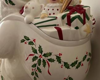 Lenox Santa Skates Cookie Jar — This charming Lenox Holiday white Santa cookie jar features detailed holly and gift motifs with gold accent mittens and hat pom-pom. Crafted from fine porcelain, it depicts Santa carrying a sack filled with toys including a teddy bear and clown. Measuring approximately 12 inches tall, this festive collector's piece adds a traditional holiday touch to any kitchen or display. The jar is in excellent condition with no visible chips or cracks, maintaining its bright and glossy finish. Made in 1999 by Lenox, this piece reflects the brand's long-standing reputation for quality holiday ceramics.