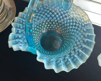 Fenton Blue Opalescent Hobnail Basket — This exquisite Fenton blue opalescent hobnail glass basket features a striking ruffled edge and a sturdy curved handle, typical of Fenton's classic design. The opalescent blue glass with hobnail texture catches light beautifully, making it a stunning decorative and collectible piece. Measuring approximately 9 inches in height, 9 inches in width, and 6 inches in length, it is ideal for display or functional use. The basket is in excellent condition with no chips, cracks, or repairs visible, reflecting careful preservation. As a vintage collectible from the renowned Fenton Art Glass Company, it represents fine American craftsmanship in art glass.
