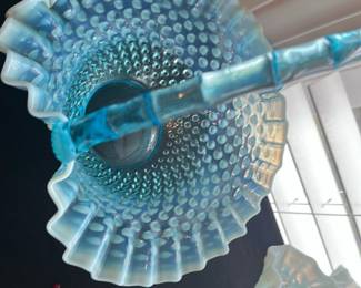 Fenton Blue Opalescent Hobnail Basket — This exquisite Fenton blue opalescent hobnail glass basket features a striking ruffled edge and a sturdy curved handle, typical of Fenton's classic design. The opalescent blue glass with hobnail texture catches light beautifully, making it a stunning decorative and collectible piece. Measuring approximately 9 inches in height, 9 inches in width, and 6 inches in length, it is ideal for display or functional use. The basket is in excellent condition with no chips, cracks, or repairs visible, reflecting careful preservation. As a vintage collectible from the renowned Fenton Art Glass Company, it represents fine American craftsmanship in art glass.