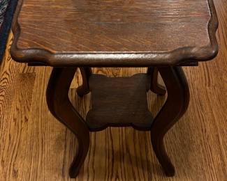 Antique Oak Accent Table — This antique oak accent table features a beautifully carved top with scalloped edges and elegantly curved legs, showcasing quality craftsmanship. The rich oak wood exhibits a warm natural finish that enhances the traditional design. Measuring approximately 22 inches high, 19 inches wide, and 18 inches deep, this compact table fits well in living room seating areas or as an accent piece. The table is in good condition with minor surface wear consistent with its age, adding to its vintage charm. Its sturdy construction and classic style make it a versatile addition to any home.